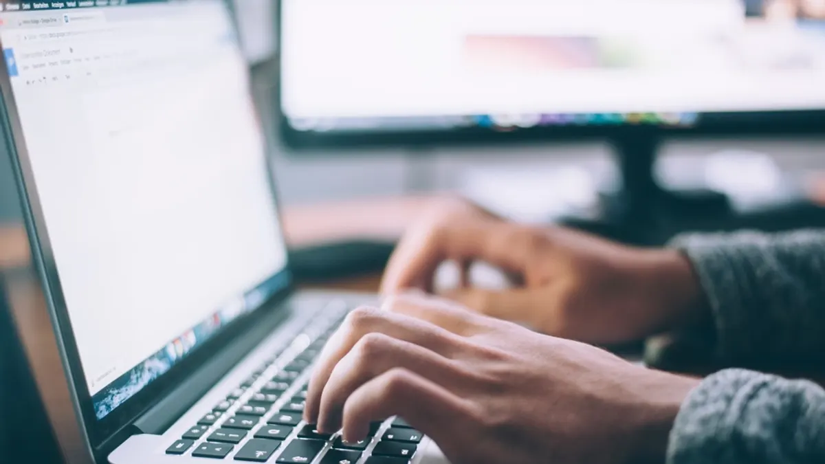 Handen typen op een laptop, tweede scherm onscherp erachter, waar je twee platformagenda's bijhoudt