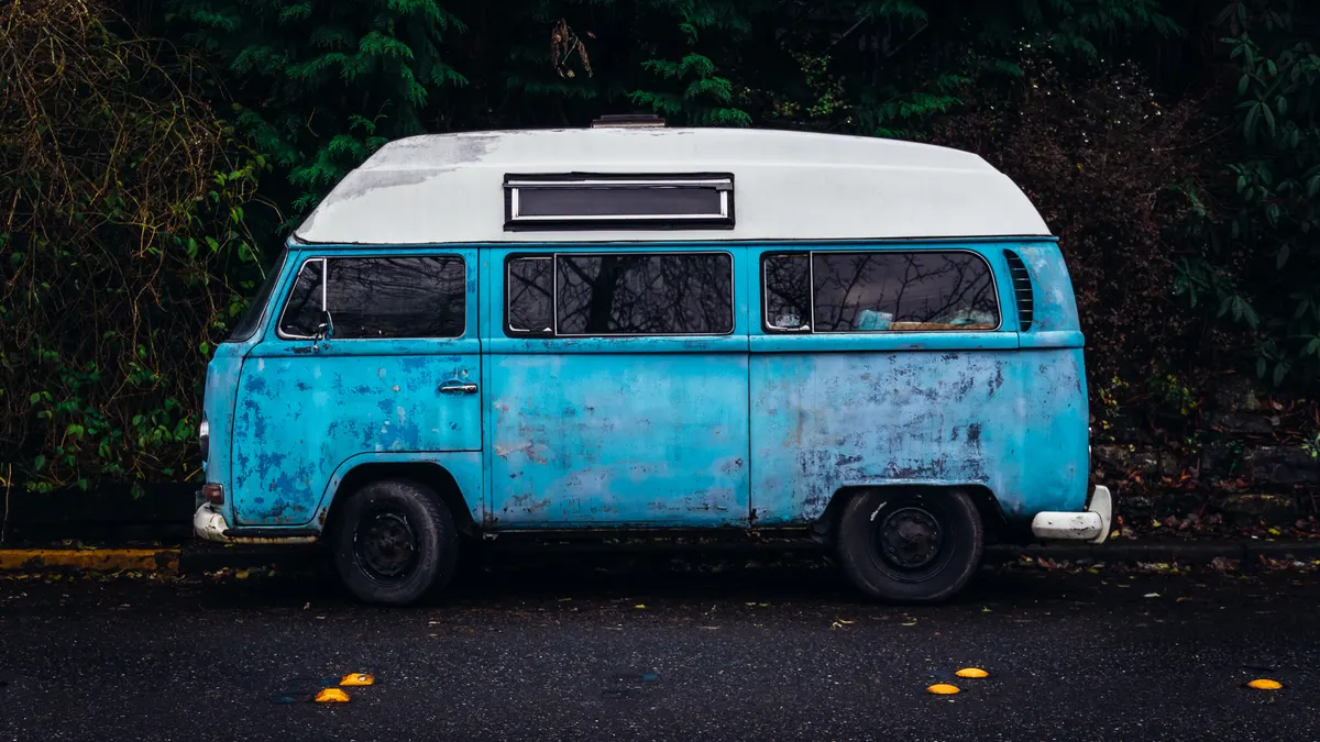 Oude blauwwitte camperbus voor een dichte heg, de camper waarvoor je een plek per nacht verhuurt