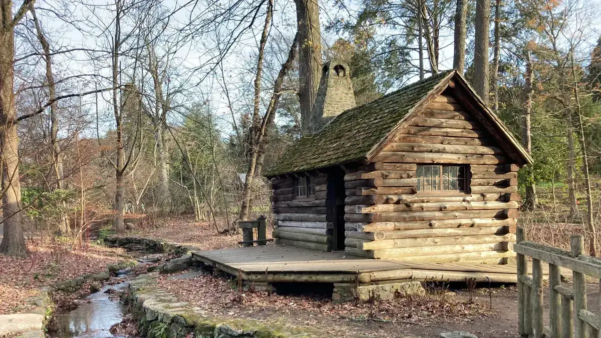 Houten recreatiechalet met mosdak aan een beekje tussen kale bomen