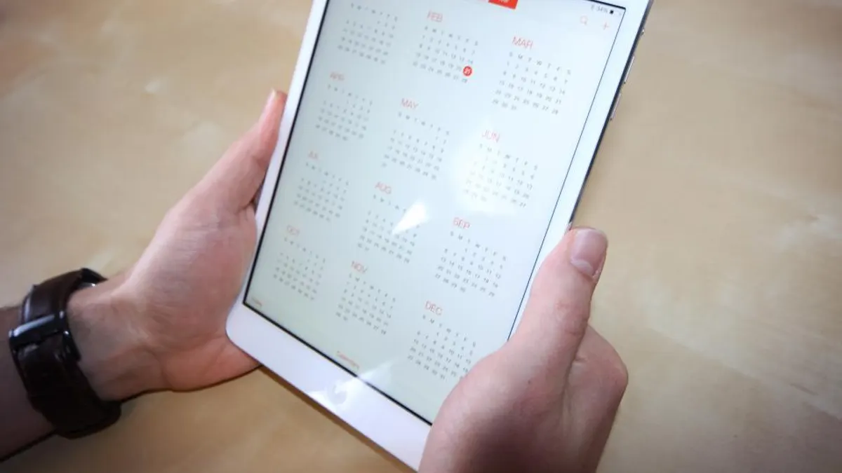 Handen met een tablet met jaarkalender om boekingsdatums te verzetten