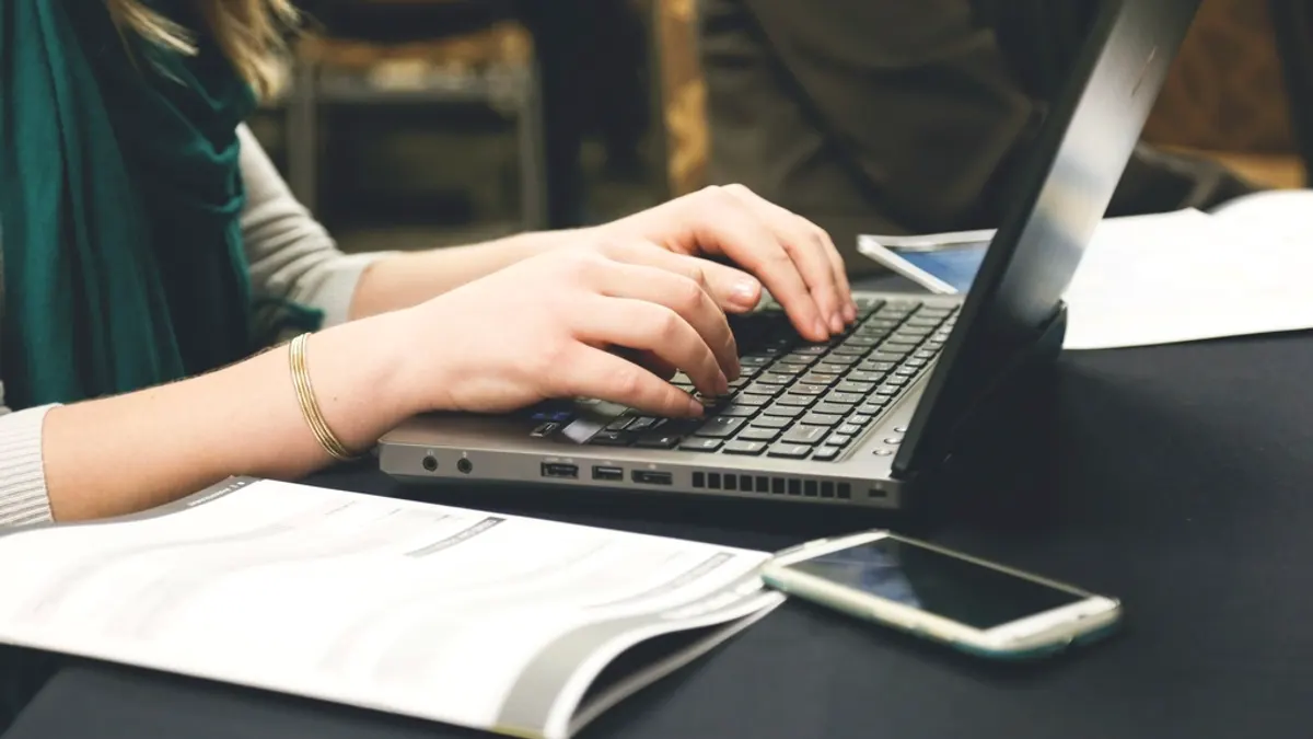 Handen typen op een laptop met papieren en een telefoon ernaast, waar je boekingsaanvragen beoordeelt