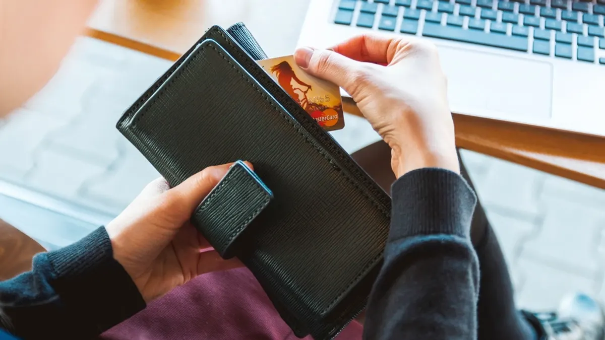 Creditcard uit een zwarte portemonnee bij een laptop, waar de gast rechtstreeks en goedkoper boekt