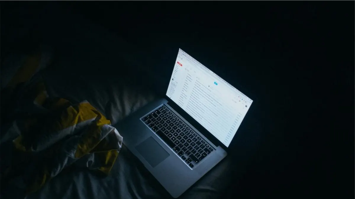 Open laptop met een mailbox op een donker bed, waar je 's avonds je bevestigingsmails nakijkt