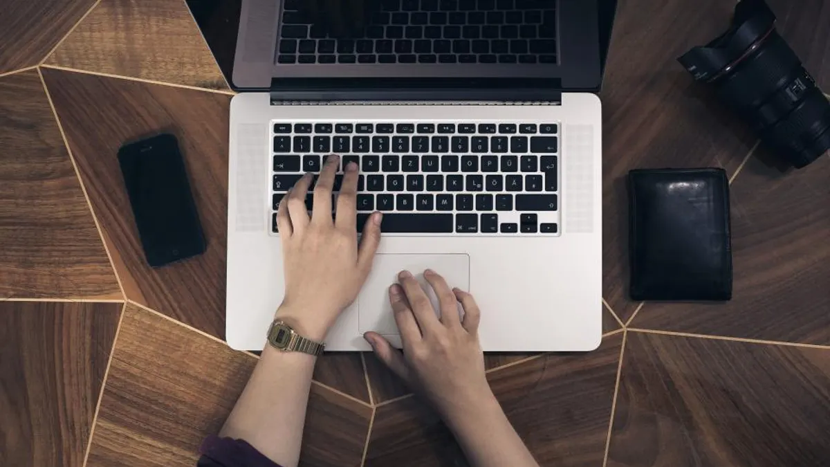 Handen typen op een zilveren laptop op een houten tafel, waar je de Micazu-kalender importeert