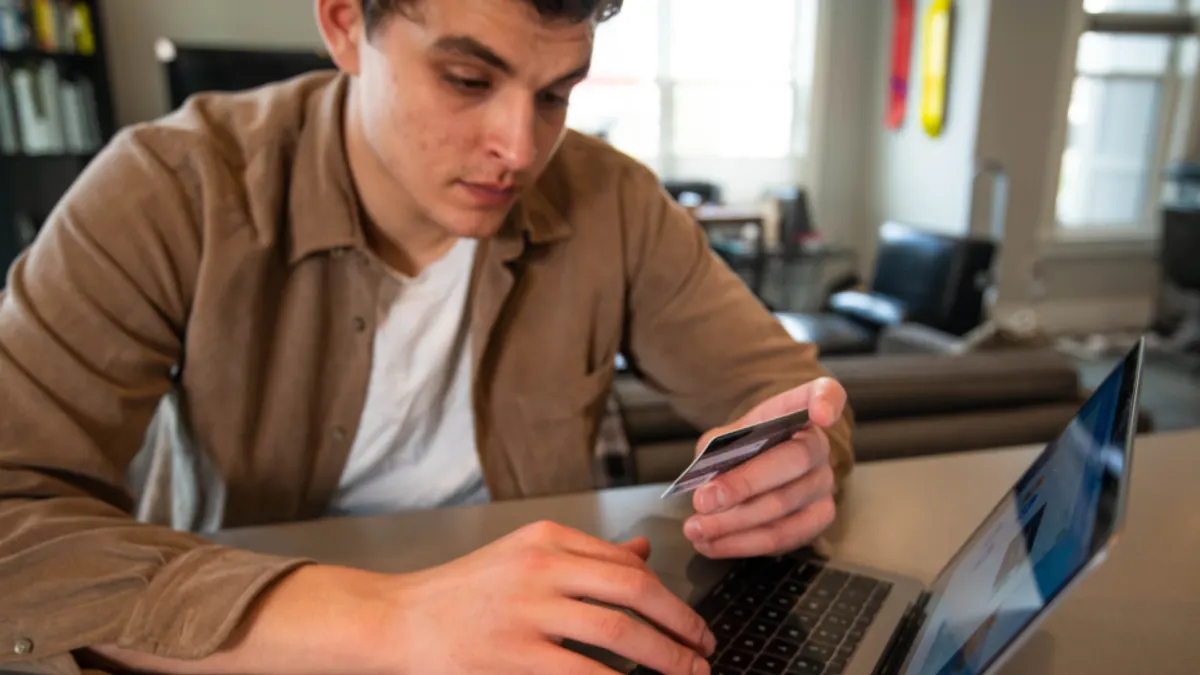 Man in bruin overhemd met een bankpas achter zijn laptop, waar je gast met iDEAL betaalt