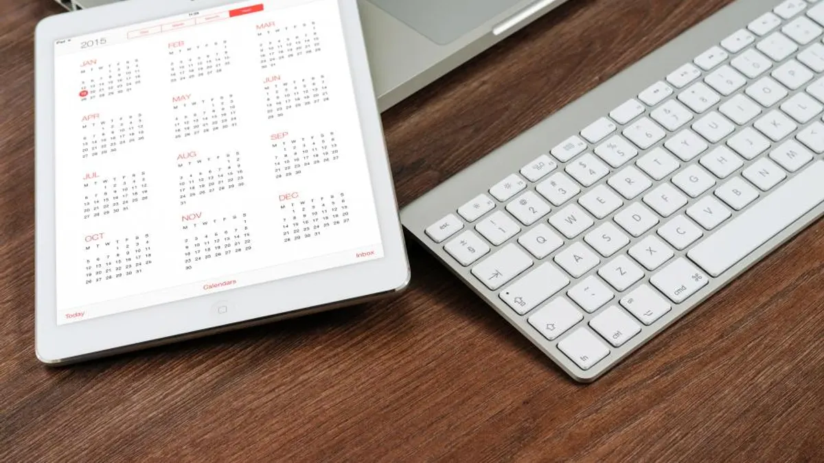 Tablet met een jaarkalender naast een toetsenbord op een houten bureau, waar je de platformagenda overzet