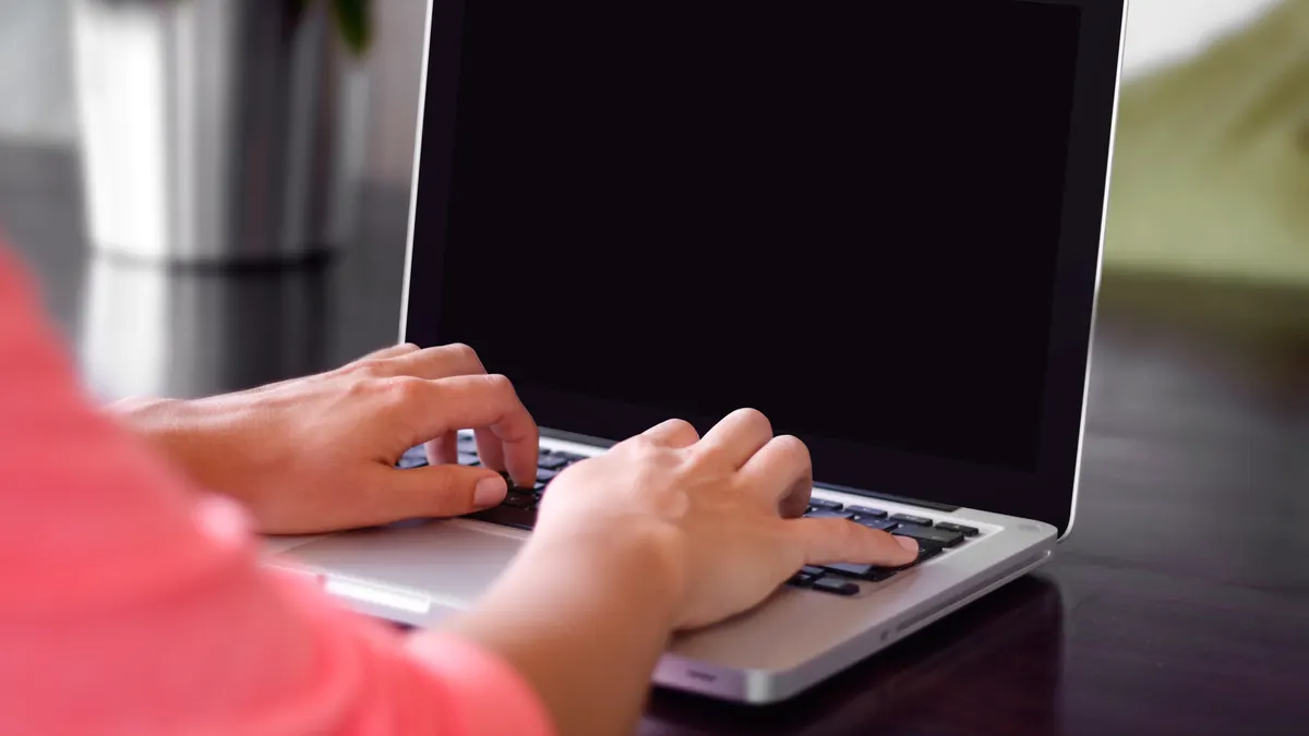 Handen typen op een zilveren laptop aan een donkere tafel, waar je een beoordeling beantwoordt