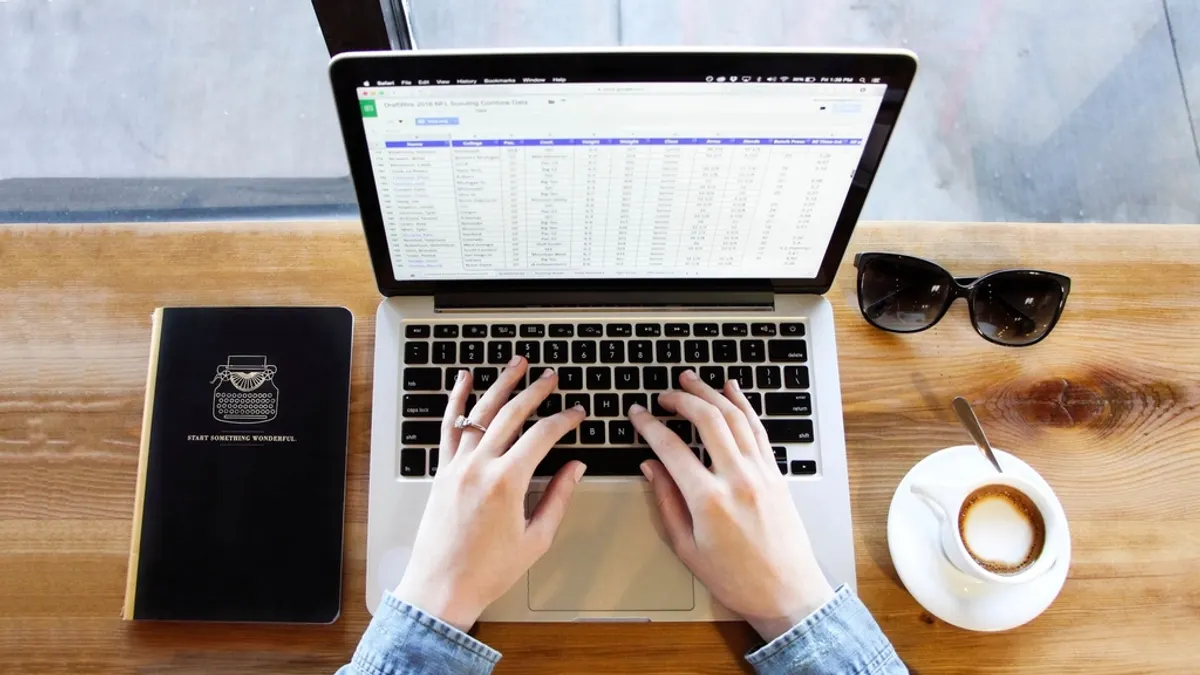 Handen typen op een laptop met spreadsheet, naast koffie, bij het berekenen van je rendement