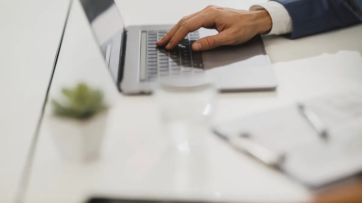 Hand in een blauw pak op een laptop naast een notitieblok, waar je je commissie narekent