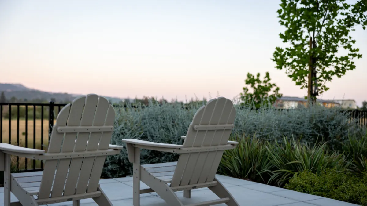 Twee lichte stoelen op een stenen terras bij schemering, de buitenruimte die je gaat verhuren