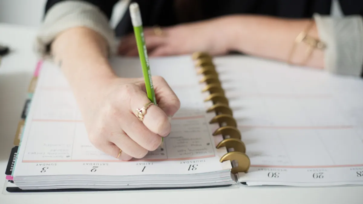 Hand noteert met potlood in een weekagenda de mailmomenten per boeking